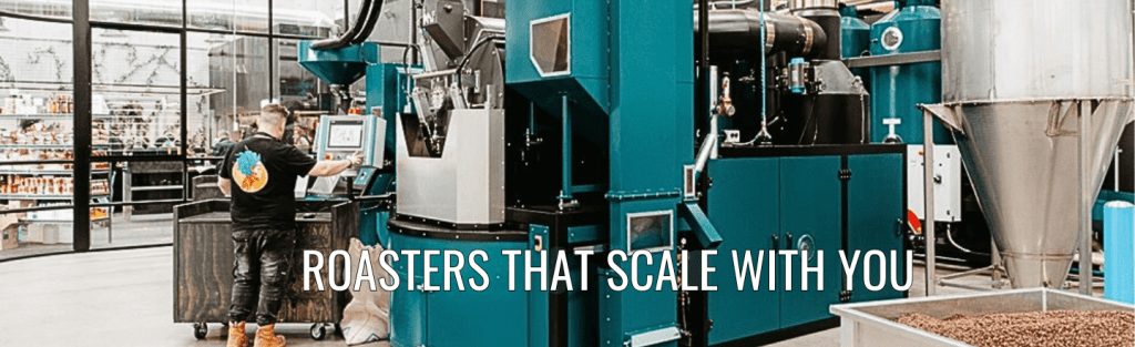 Coffee roaster operating a teal IMF roasting system in a modern glass-walled facility with bags of green coffee.