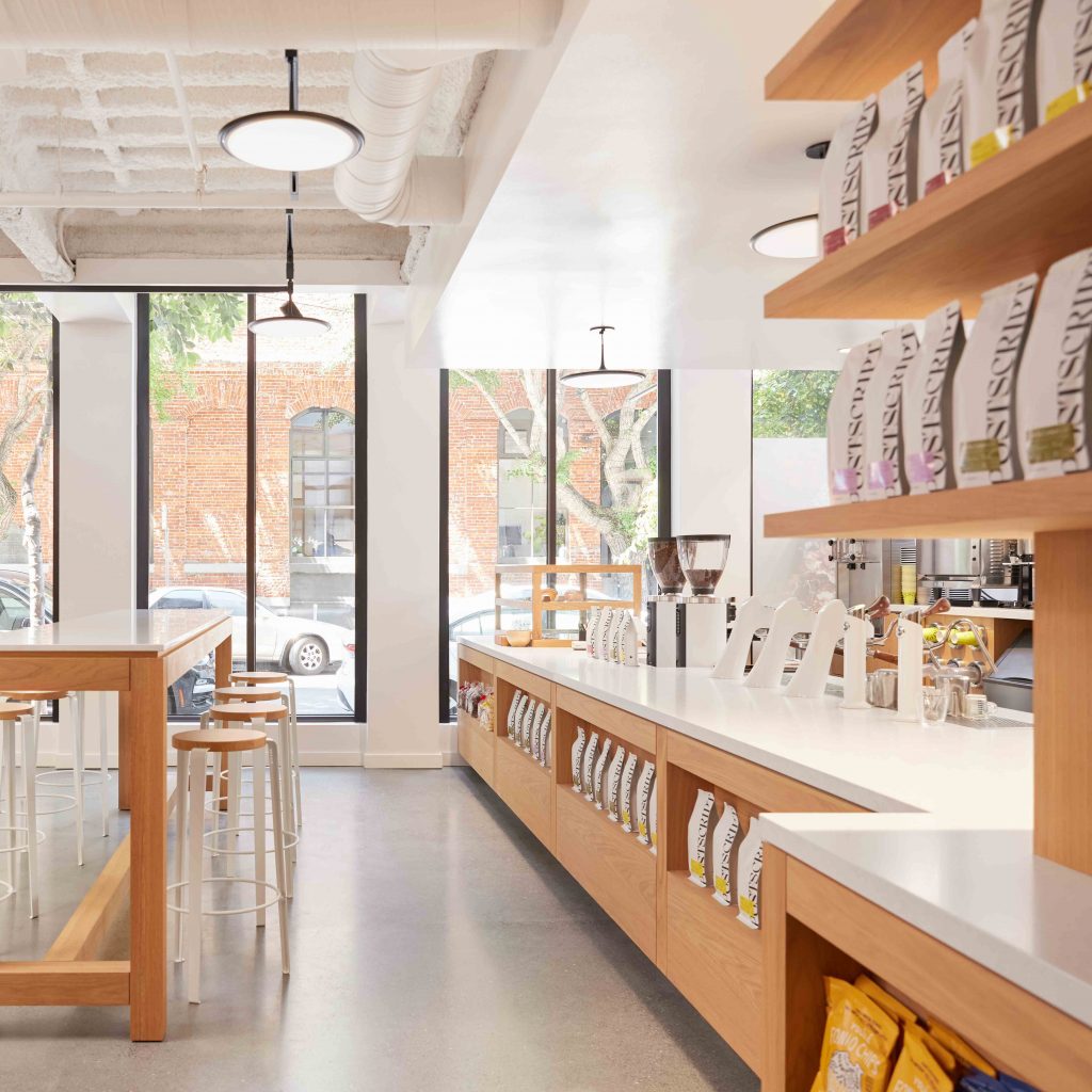 Postscript cafe seating area with white oak shelving displaying Siscript coffee bags, natural light, San Francisco, CA